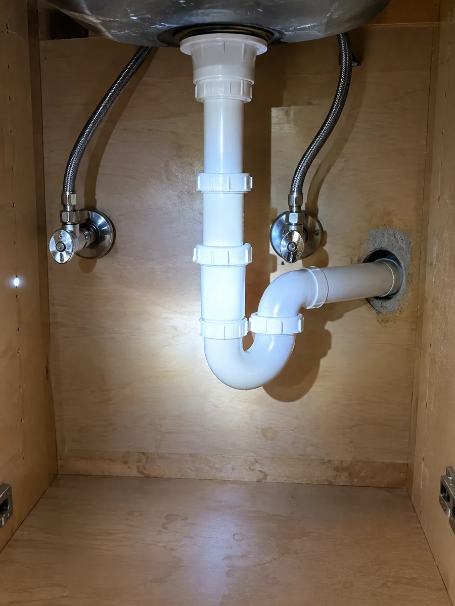 The inside of a sink base cabinet showing the P trap, two shutoff valves and where the drain enters the wall
